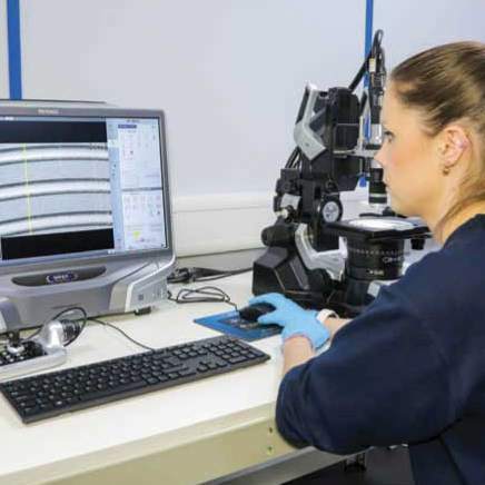 A woman inspects a metal component using a microscope